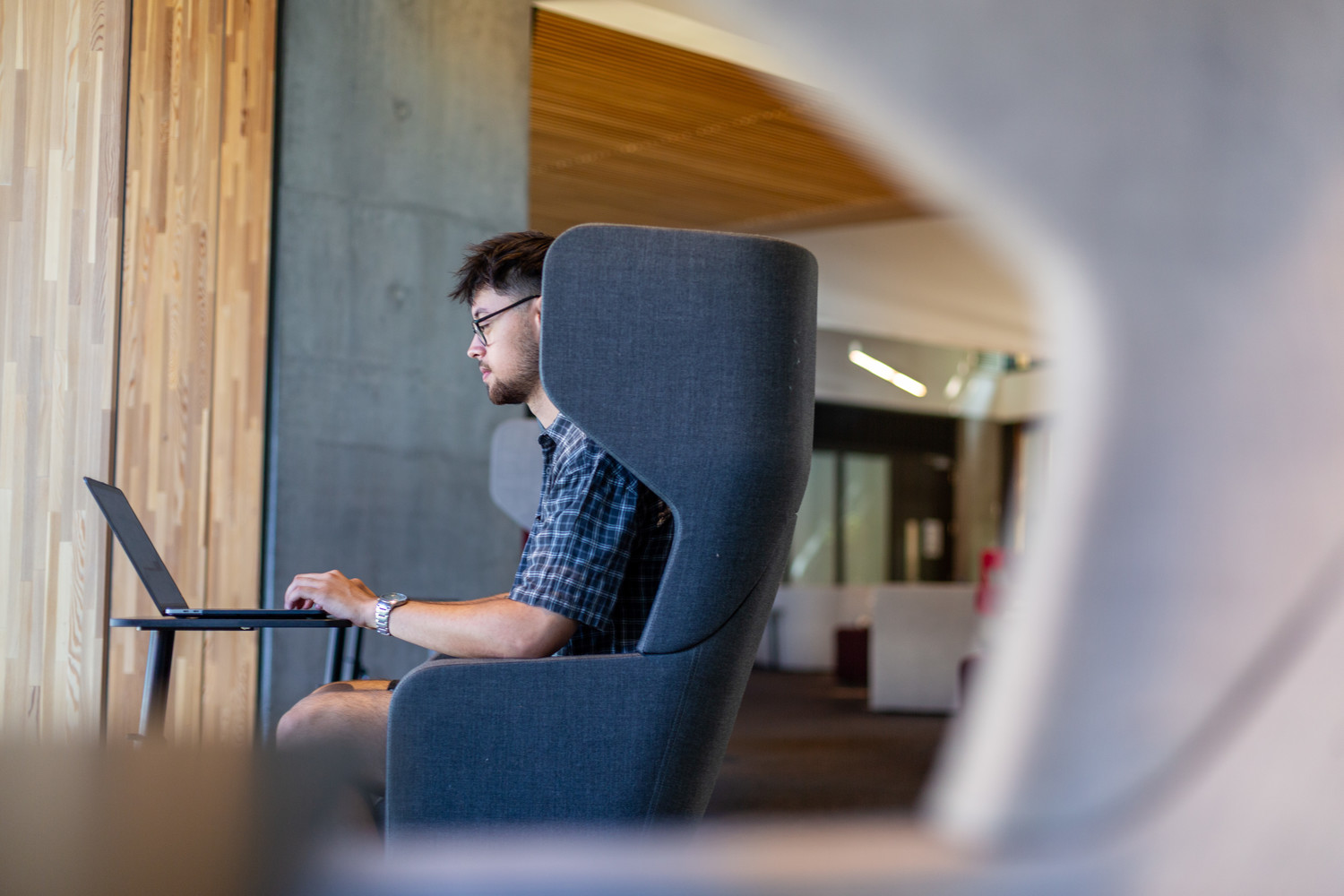 A student is concentrating on his laptop sat on modern seating