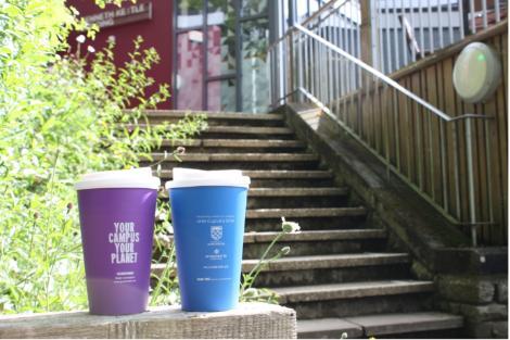 Two reusable coffee cups on a wall with steps and cafe in the background