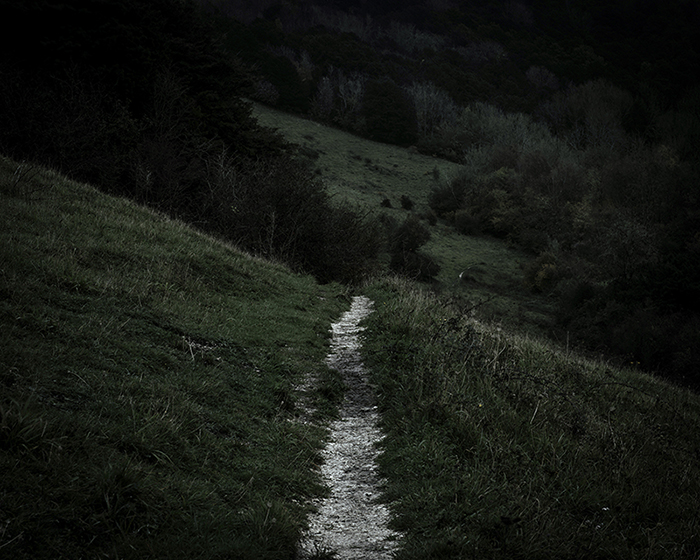 Photograph of a dark path disappearing across the hills