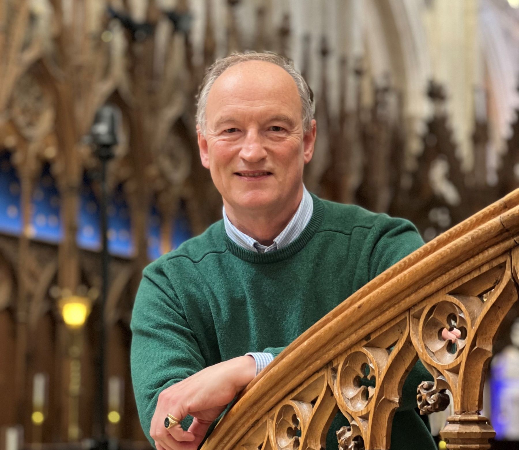 Middle aged man with green jumper looking over ornate banister rail