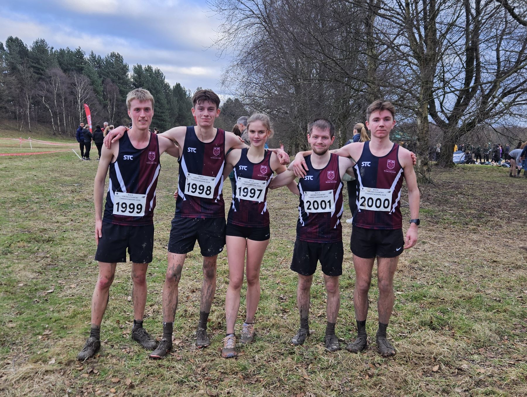 Five muddy cross country runners pose for photo after race
