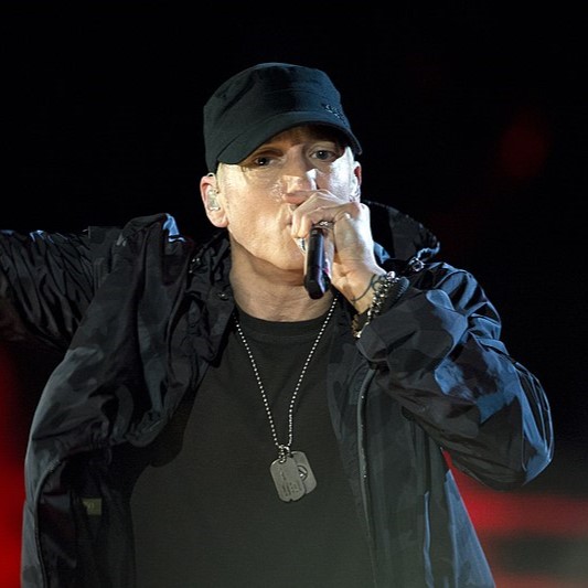 rapper Eminem on stage with mic. Wearing dark baseball cap.