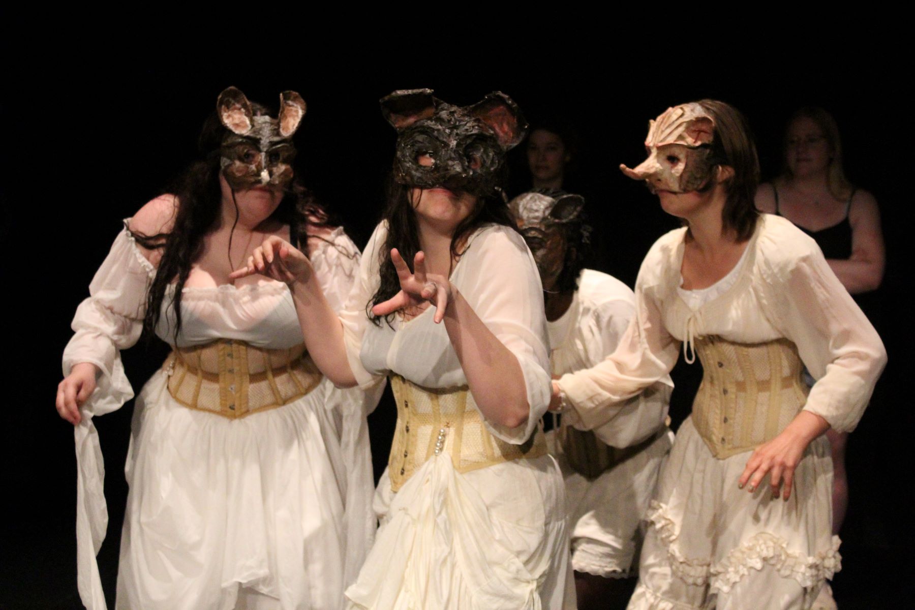 Women in white dresses and grotesque masks