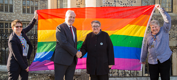 Two people shaking hands in front of a rainbow Pride flag