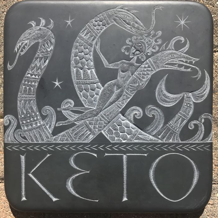 Square black plaqu white carved lettering spelling KETO below a mythical sea creature and sea goddess