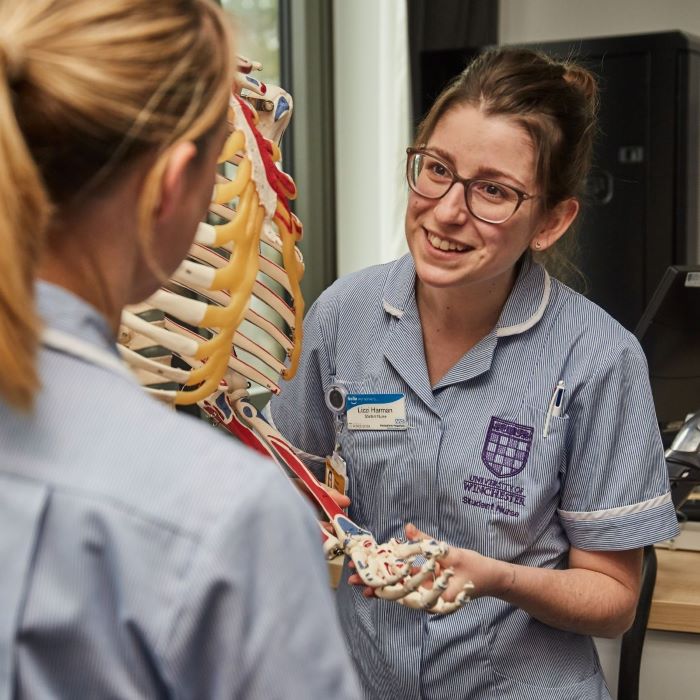 Two female student nurses talking next to skeleton. One has back to camera