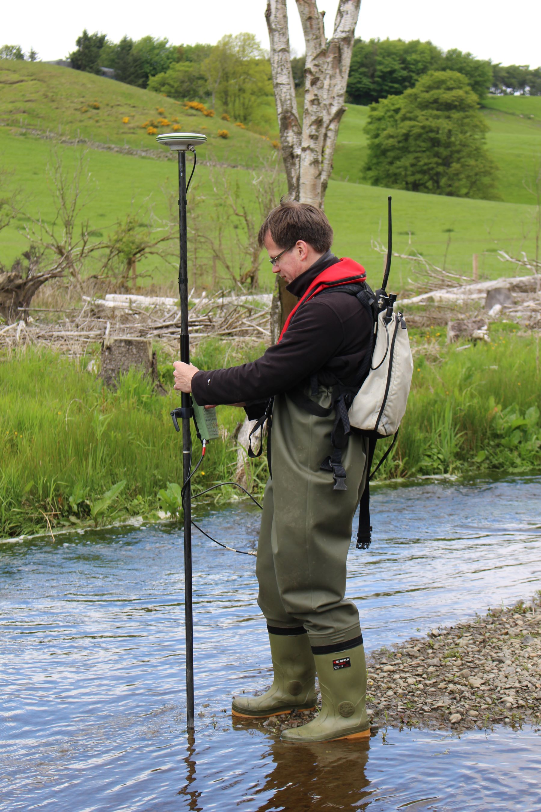 Man in waders with measuring stick in shallow stream