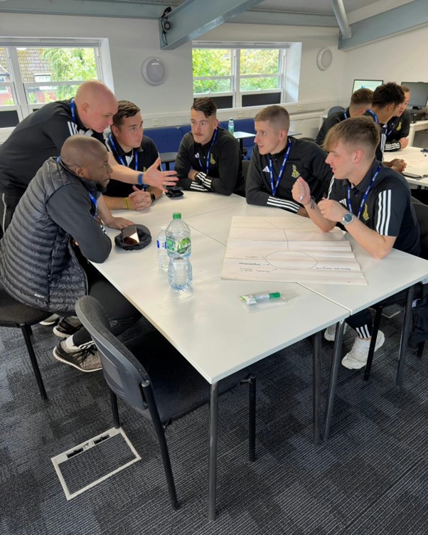 Young men in tracksuits sat around a table in discussion