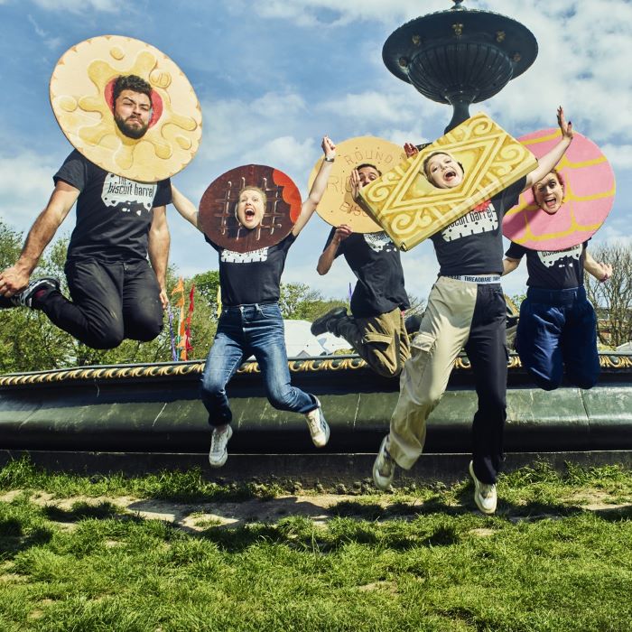 Five people with biscuit headdresses leaping in the air