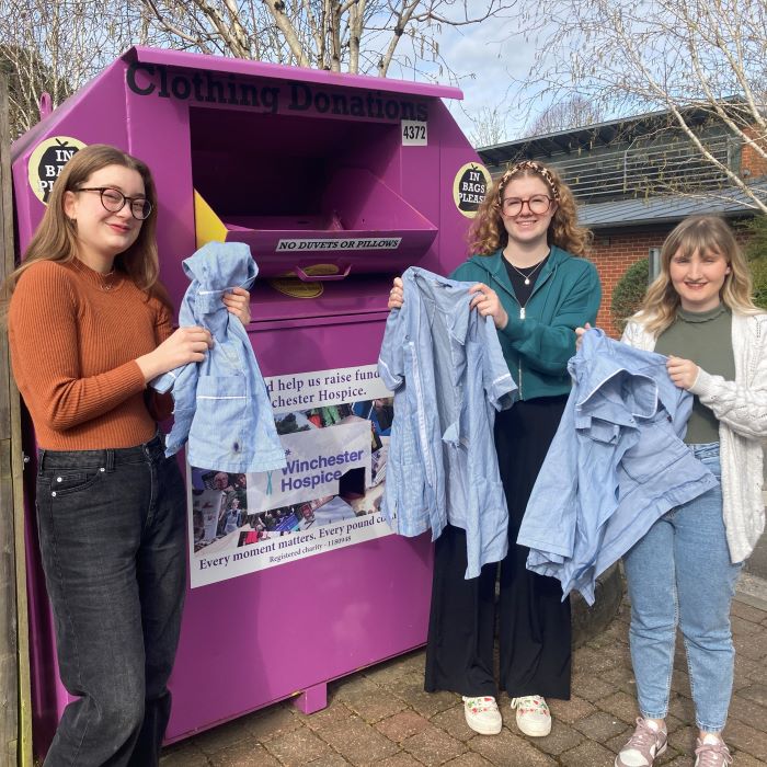 Three young women putting clothes into a pink cloth recycling bin