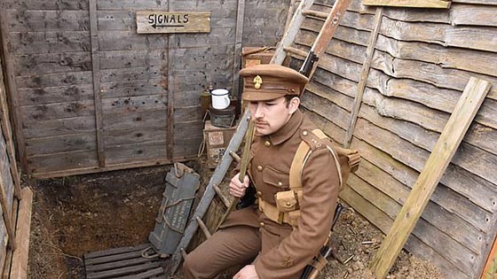 Male student in WWI uniform sitting in trench