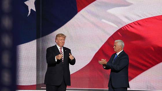 Donald Trump stabnding with another man in front of a US flag backdrop