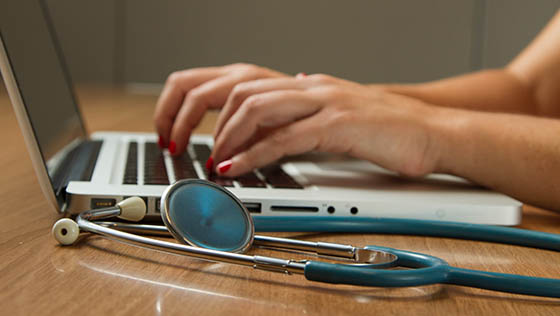 Close up of hands typing on a laptop with stethoscope on the desk