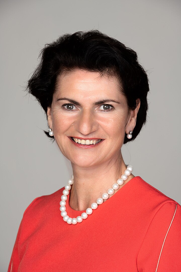 Woman with dark hair, red jumper and pearls
