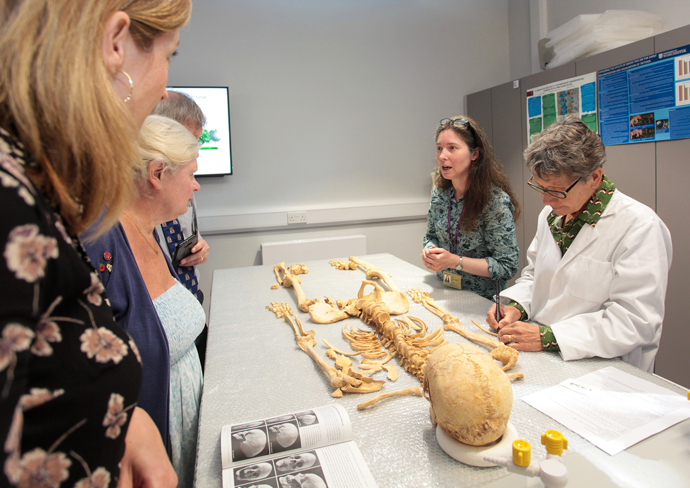 An academic explaining forensic science to members of the public in a laboratory, with a skeleton laid out on a table