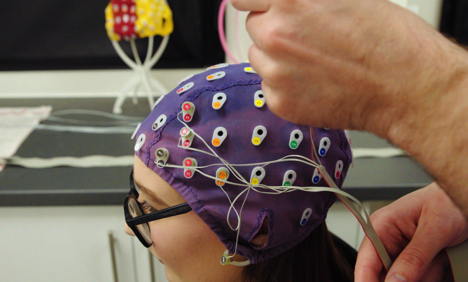 Student with brain monitoring instruments attached to head cap