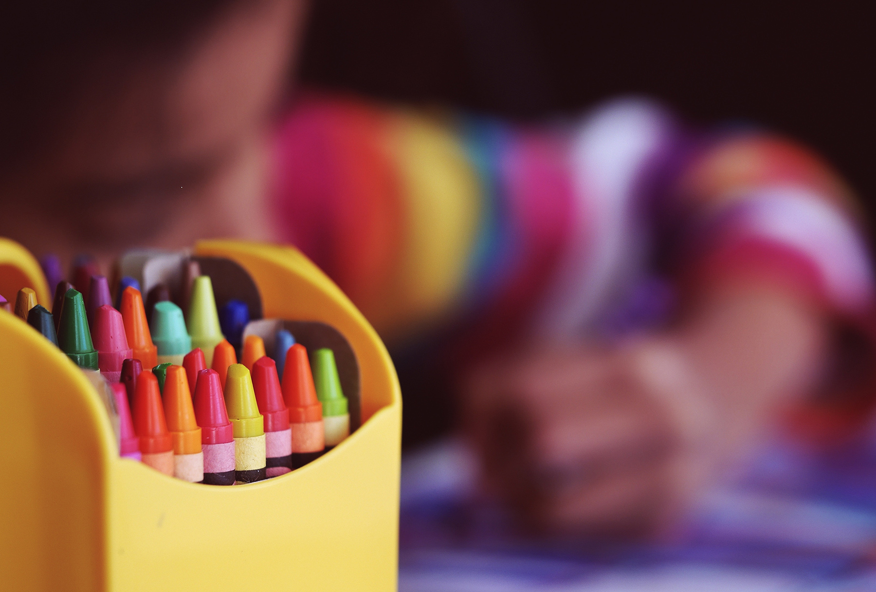 Crayons in a box with a child behind