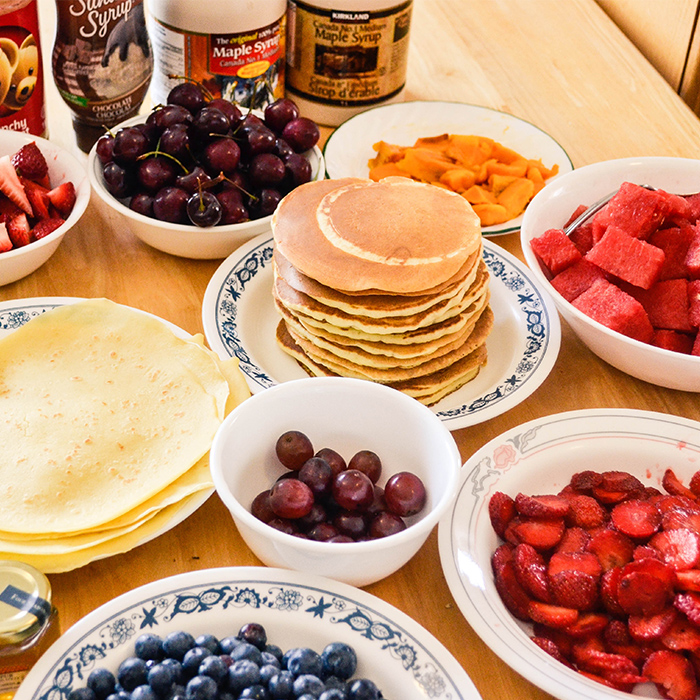 Pancakes and fruit in plates and bowls on a table