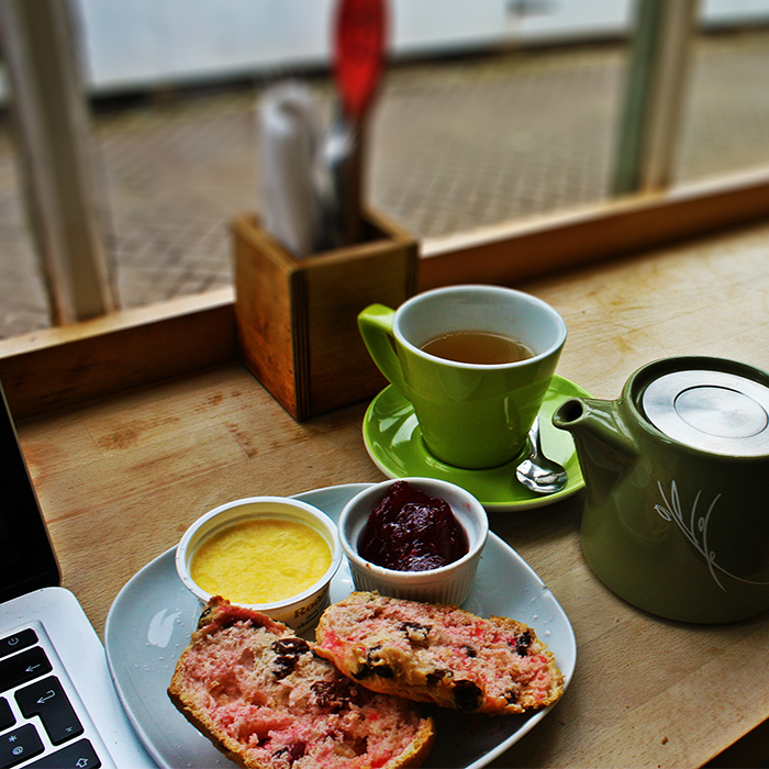 Food and a mug of tea on a table next to a laptop