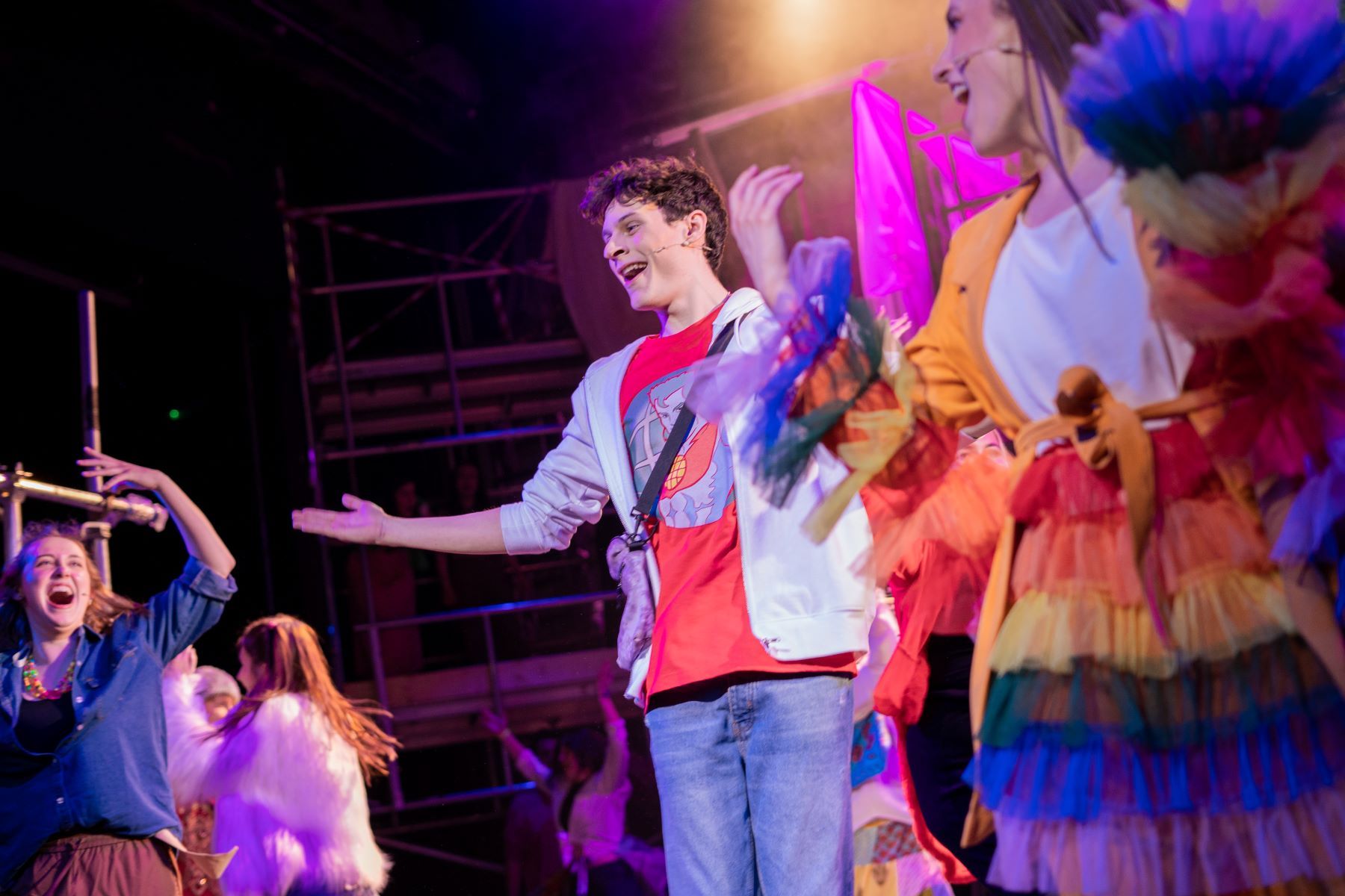 Young male actor on stage with colourfully dressed cast members in the backgroun