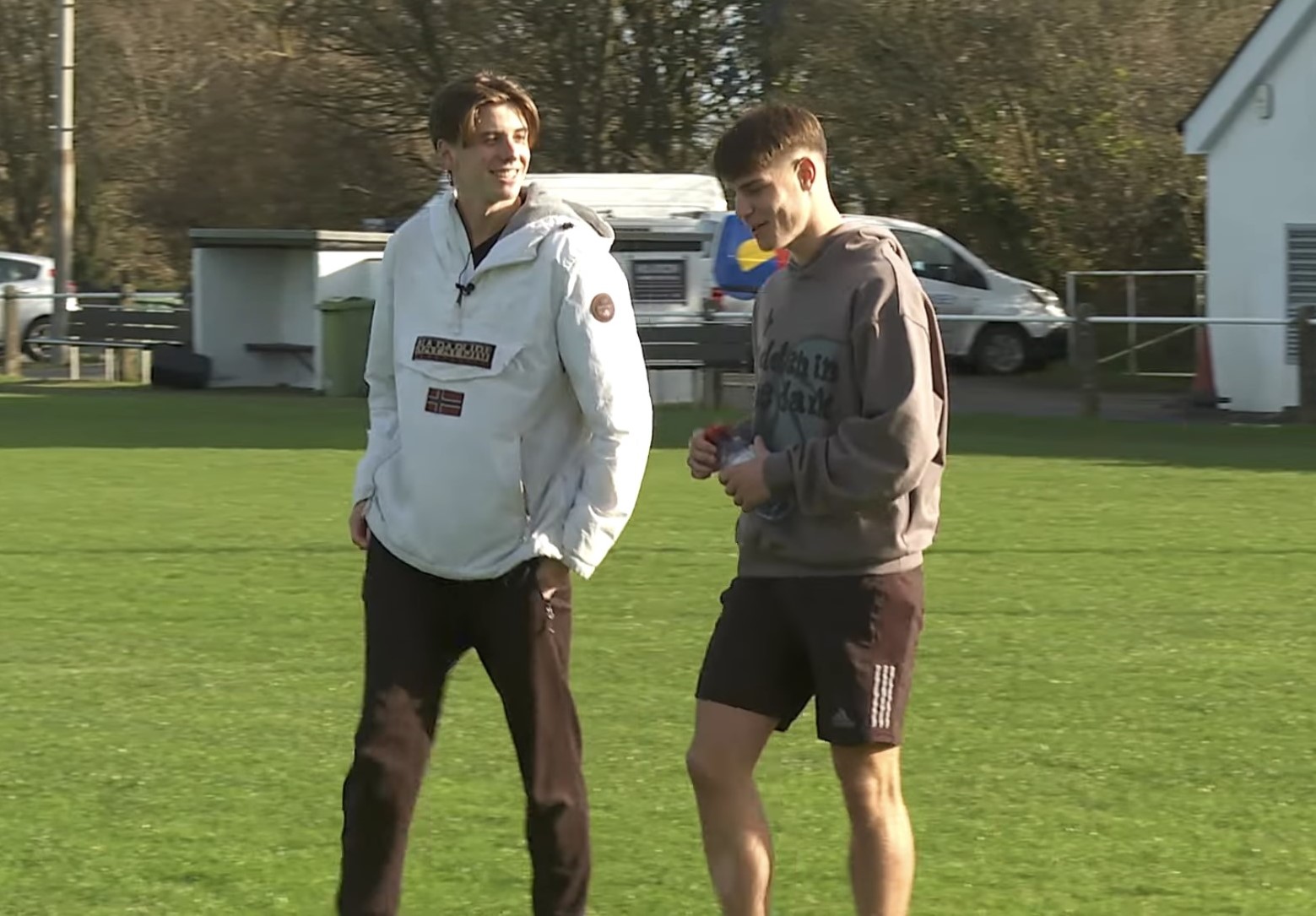 Two young men walk across football field talking