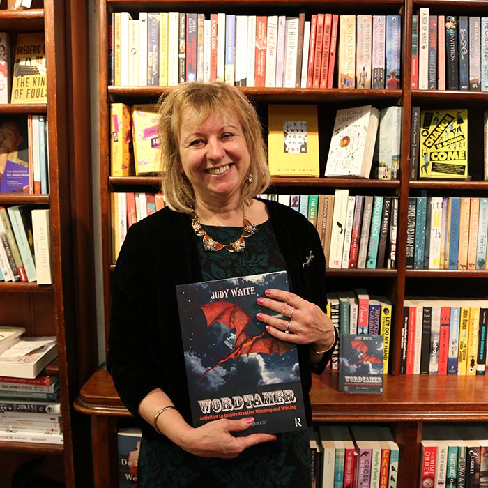 Woman in black dress holding a book standing in front of bookcase