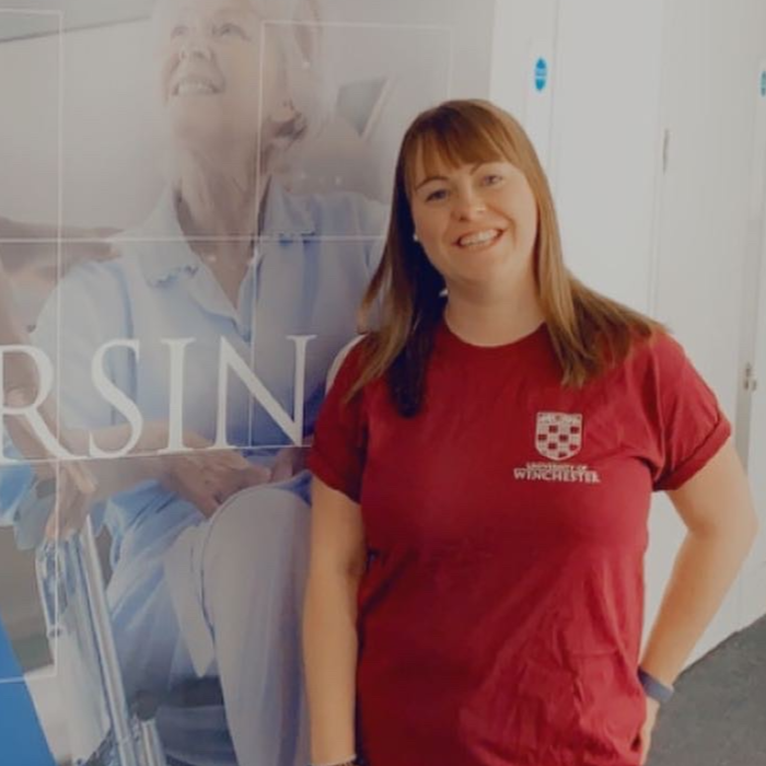 Student in red shirt smiling in front of banner saying Nursing