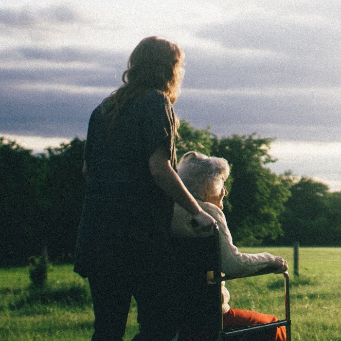 A young woman pushing an older woman in a wheelchair on the grass towards the sunlight