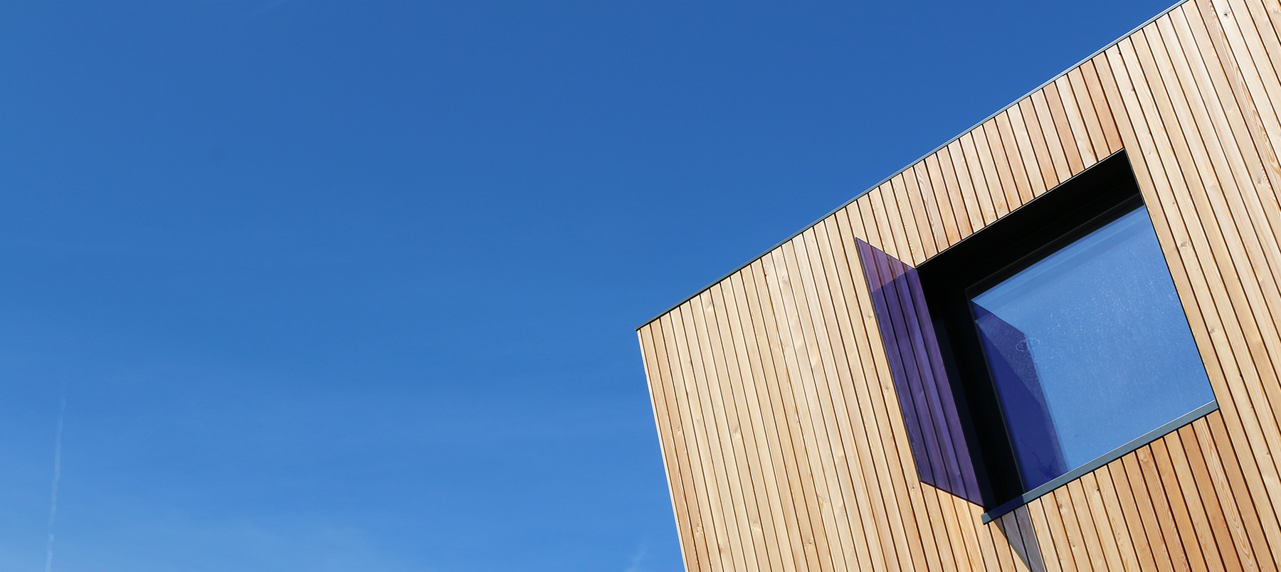 Top of timber clad contemporary building against a bright blue sky