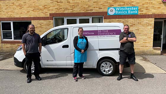 Three people standing by a van in front of the Winchester Basics Bank