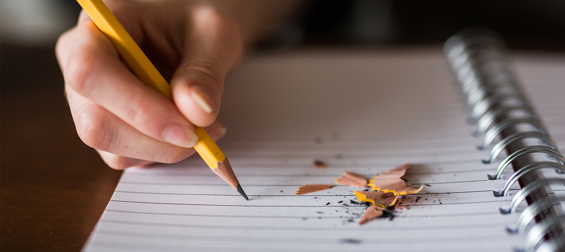 Person writing in a notepad with a pencil, pencil sharpenings on the paper
